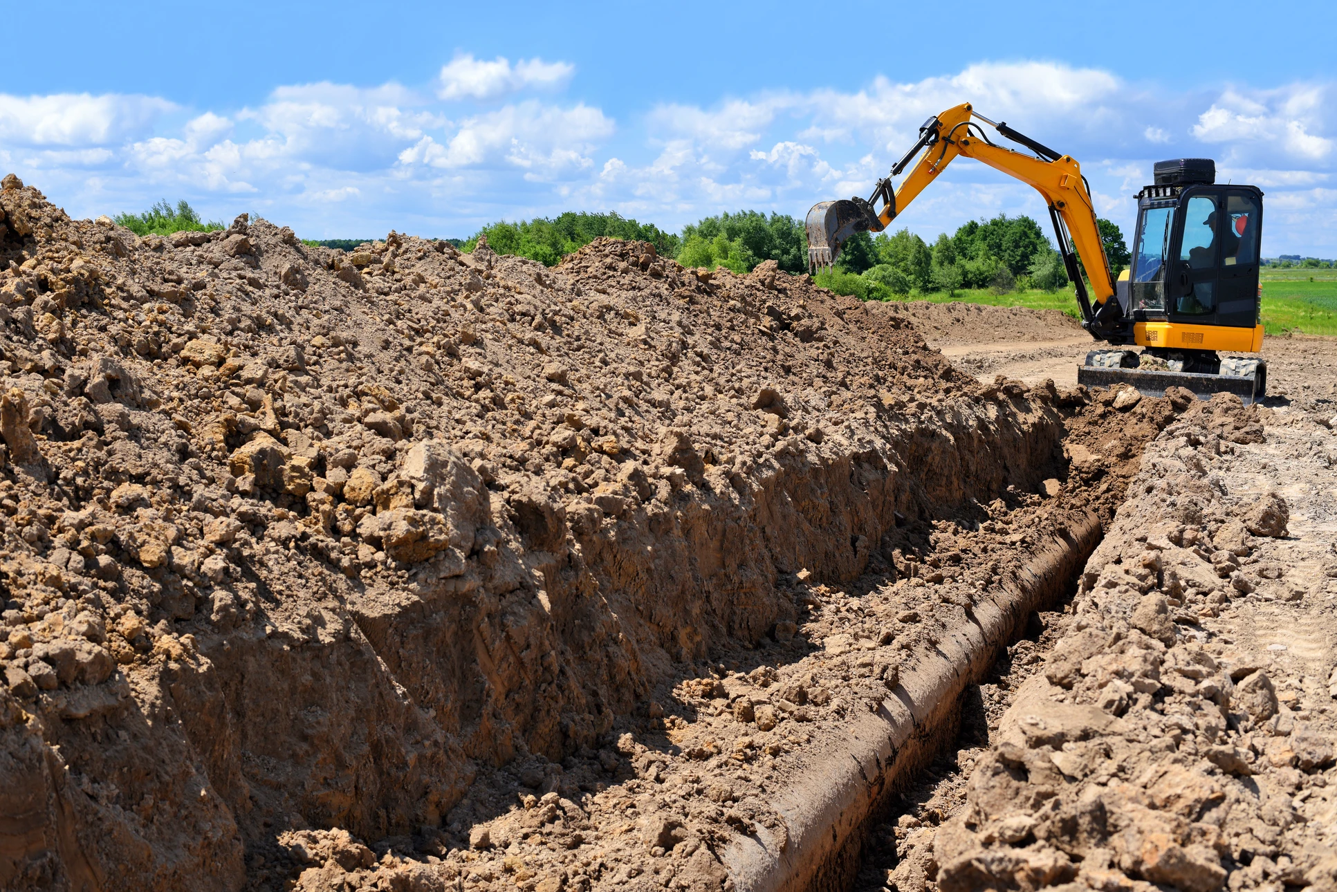 Chantier de canalisation en extérieur avec ouvrier en gilet haute visibilité et casque jaune installant une vanne sur conduite d'eau